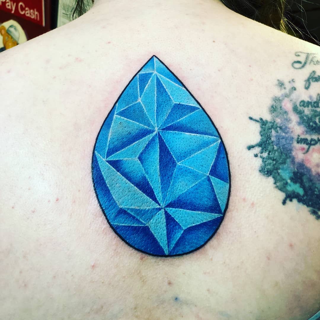 Geometric tattoo of a blue teardrop-shaped gemstone inspired by Lapis Lazuli from Steven Universe, located on the upper back